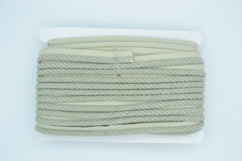 Pu&ograve; includere: Un rotolo di cordoncino intrecciato beige e bianco, perfetto per progetti di artigianato.