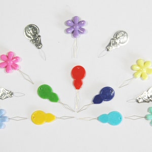 May include: Assortment of colourful plastic needle threaders with different shapes, including flowers and teardrops. The threaders have a small metal loop at the end for threading needles.