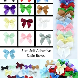 Peut inclure: Assortiment de nœuds en satin autocollants de 5 cm dans différentes couleurs, notamment noir, rouge, bleu, vert, violet, blanc, jaune, rose, bleu clair et gris. Les nœuds sont disposés en grille et affichés sur un fond blanc. 5cm Nœuds en Satin Autocollants.