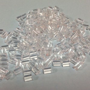 Peut inclure: Un grand tas de perles en plastique transparent, chaque perle est un petit cylindre avec un trou au centre.