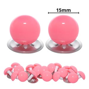 Puede incluir: Un conjunto de ojos de seguridad esf&eacute;ricos de color rosa con un acabado liso y brillante. Cada ojo presenta un domo rosa de 15 mm de di&aacute;metro unido a un poste de pl&aacute;stico blanco y una base de arandela met&aacute;lica circular.