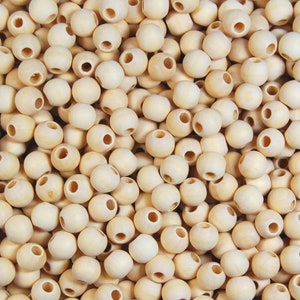 May include: A close-up image of a pile of natural wood beads. The beads are round and have a hole through the centre. They are a light beige colour.