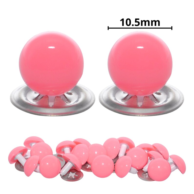 Puede incluir: Dos ojos de seguridad de pl&aacute;stico rosa con arandelas de metal plateado, cada uno de 10,5 mm de di&aacute;metro, colocados sobre un mont&oacute;n disperso de ojos de seguridad rosas id&eacute;nticos sobre un fondo blanco para proyectos de manualidades.