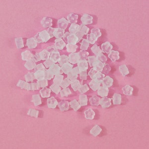 Könnte beinhalten: Ein Haufen durchsichtiger Ohrstecker aus Kunststoff in Blumenform auf rosa Untergrund.