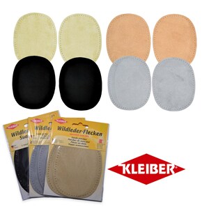 Könnte beinhalten: Sortiment aus Wildleder-Flicken in verschiedenen Farben, darunter Schwarz, Beige, Hellbraun und Grau. Die Flicken sind oval geformt und haben einen genähten Rand. Die Verpackung enthält den Text "Wildleder-Flecken" und den Markennamen "KLEIBER".