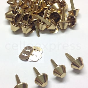 Peut inclure: Un tas de rivets en métal coniques de couleur dorée avec une extrémité pointue. Il y a aussi trois rivets individuels et deux boucles en métal dorées.