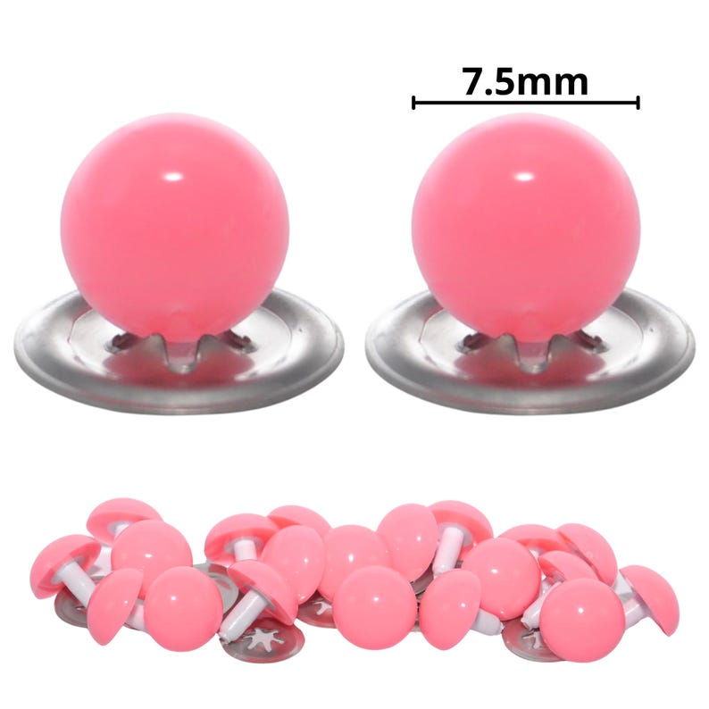 Puede incluir: Una colecci&oacute;n de ojos de seguridad de pl&aacute;stico rosa con arandelas de metal plateado. Dos piezas individuales se muestran arriba con una l&iacute;nea de medici&oacute;n que indica un di&aacute;metro de 7,5 mm. El resto de las piezas est&aacute;n esparcidas en la parte inferior.
