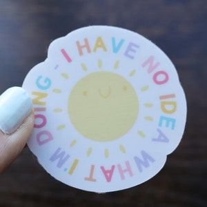 May include: A white round sticker with a yellow sun in the center and the text "I HAVE NO IDEA WHAT I'M DOING" around the sun. The text is in rainbow colors.