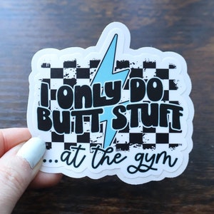 May include: A white sticker with a black and white checkered background and the text "I only do butt stuff...at the gym" in black and blue. A blue lightning bolt is in the center of the sticker.