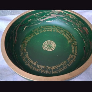 May include: A round green bowl with a gold-painted rim and interior. The center features a gold spiral, surrounded by gold text that reads: Gaia! Ancient Mother of earth and sky, ground my heart, quiet my mind, and teach me to walk gently upon your living body; may I always honour your abundance, care and peace be with me in this moment.