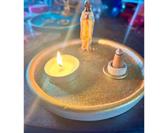May include: A gold-coloured ceramic incense burner with a small white candle, a cone incense holder, and a small figurine of a woman in a white robe.