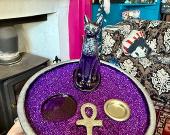 May include: A purple glitter incense burner with a silver rim. It features a black cat figurine, an ankh symbol, and two small dishes.