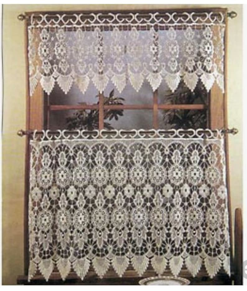 Pu&ograve; includere: Tende in pizzo bianco con un delicato motivo floreale. Le tende sono appese a una finestra con una cornice in legno.