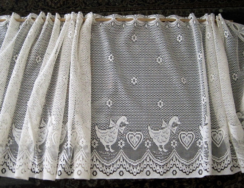 Pu&ograve; includere: Tenda di pizzo bianco con un motivo di anatre e cuori. La tenda &egrave; realizzata in un tessuto delicato e trasparente e ha un bordo a festoni.