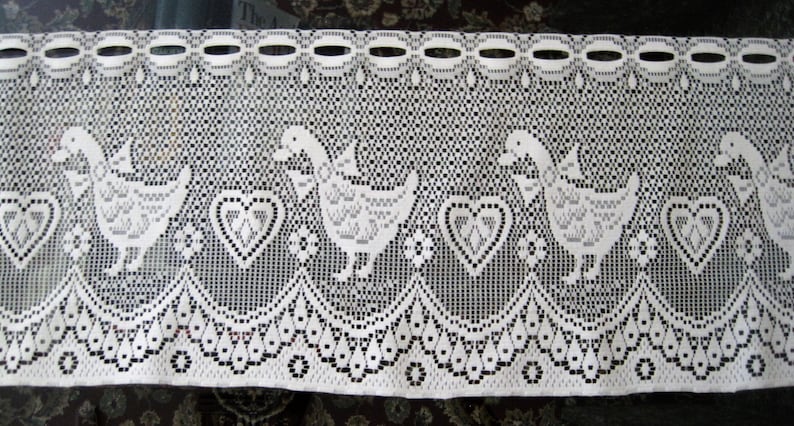Pu&ograve; includere: Un tendaggio in pizzo bianco con un motivo ripetitivo di anatre e cuori. Il tendaggio ha un bordo inferiore a forma di conchiglia.