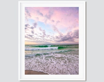May include: A photograph of a beach scene with a pink and blue sky, white clouds, and turquoise waves crashing on the shore.