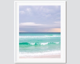 May include: A photograph of a beach scene with turquoise water and white sand. The sky is a light blue with white clouds.