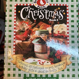 May include: A green and white checkered book titled "Gooseberry Patch Christmas Book 3" with a red bird and a jar of chocolate cookie mix on the cover. The book features old-fashioned recipes, handmade holiday gifts, and ideas for frosty fun.