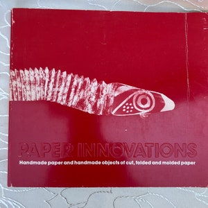 May include: A red book with the title "PAPER INNOVATIONS" and the subtitle "Handmade paper and handmade objects of cut, folded and molded paper". The cover features a white stylized image of a fish.