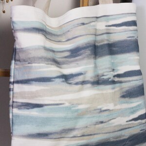 May include: A white tote bag with blue and gray watercolor-style stripes. The bag has two long straps.