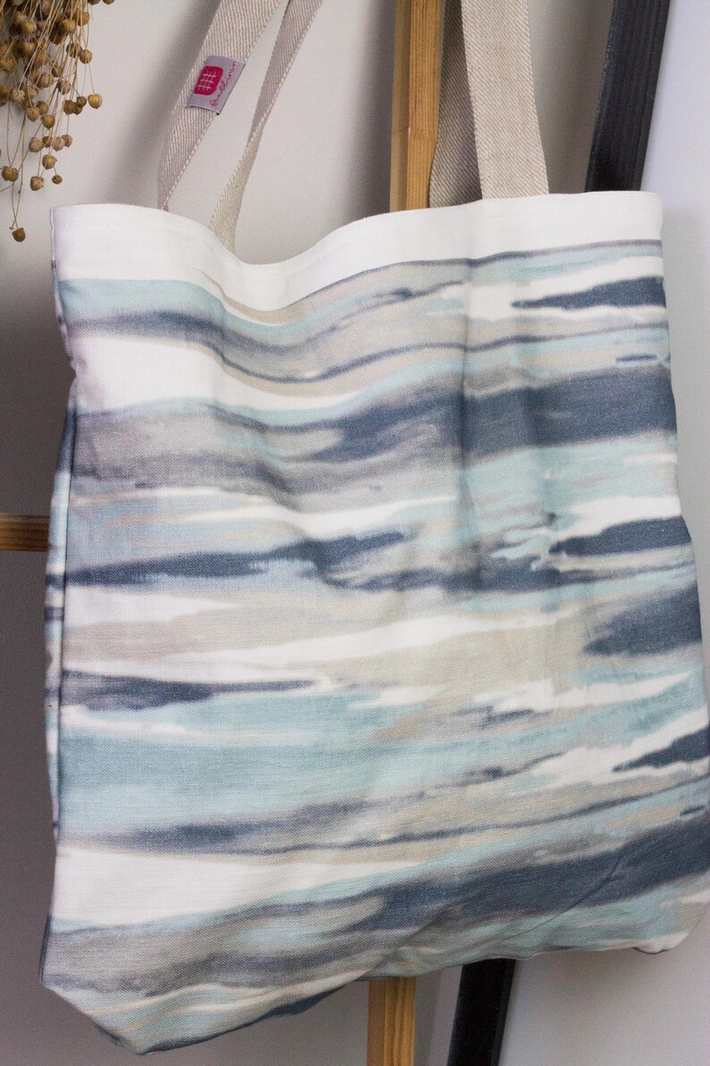 May include: A white tote bag with blue and gray watercolor-style stripes. The bag has two long straps.