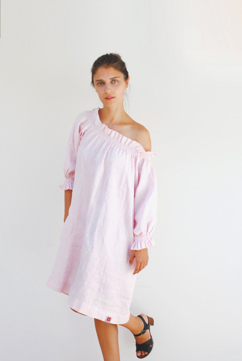 May include: A pink off-the-shoulder linen dress with ruffled sleeves. The dress is knee-length and has a relaxed fit.