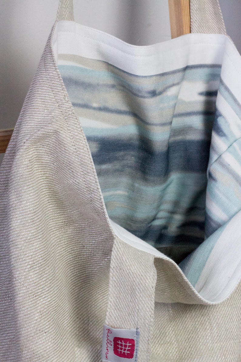 May include: A beige linen tote bag with a blue and white striped lining. The bag has a small label that says "RedLinen".