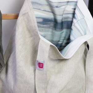 May include: A beige linen tote bag with a white lining and a blue and gray abstract print. The bag has a small red label with the text "#relleno" on it.