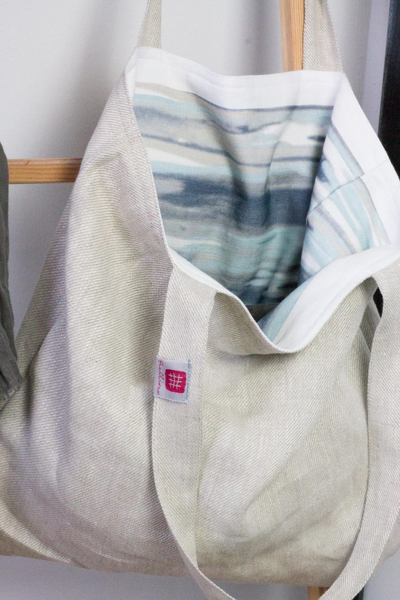 May include: A beige linen tote bag with a white lining and a blue and gray abstract print. The bag has a small red label with the text "#relleno" on it.