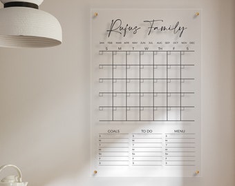 May include: A clear acrylic dry erase calendar with the text "Rufus Family" at the top. The calendar has a grid for each month of the year, with spaces for writing in appointments and events. Below the calendar are sections for goals, to do, and menu.