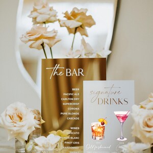 May include: A gold sign with the text "The Bar" lists beer and wine options. A second sign displays "Signature Drinks" with illustrations of cocktails. Floral arrangements and a mirror complete the elegant bar setup.