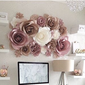 K&ouml;nnte beinhalten: Eine Wand, die mit gro&szlig;en Papierblumen in Rosat&ouml;nen und Cremefarben dekoriert ist. Die Blumen sind in einer Gruppe angeordnet und schaffen einen sch&ouml;nen und eleganten Hintergrund.