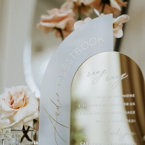 May include: A frosted glass arch with the words "Audio Guestbook" and "ring ring" written in gold lettering. The arch is placed on a gold mirror with instructions for guests to record a message for the couple.