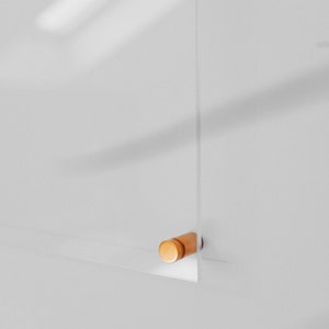May include: A clear acrylic panel with a small, cylindrical wooden accent. The panel is mounted on a white wall, and the wooden accent is a light brown color. The image is a close-up shot.