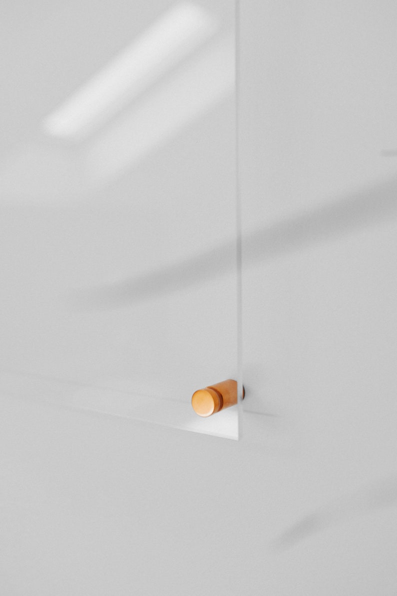 May include: A clear acrylic panel with a small, cylindrical wooden accent. The panel is mounted on a white wall, and the wooden accent is a light brown color. The image is a close-up shot.