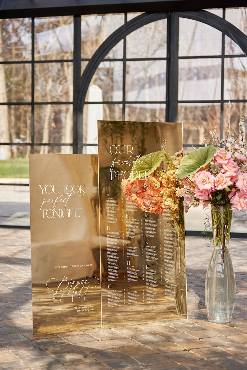 May include: Gold mirrored wedding seating chart with the text "YOU LOOK perfect TONIGHT" and "OUR favorite PEOPLE". The chart includes a list of names and is decorated with flowers. The wedding is in Draper, Utah.