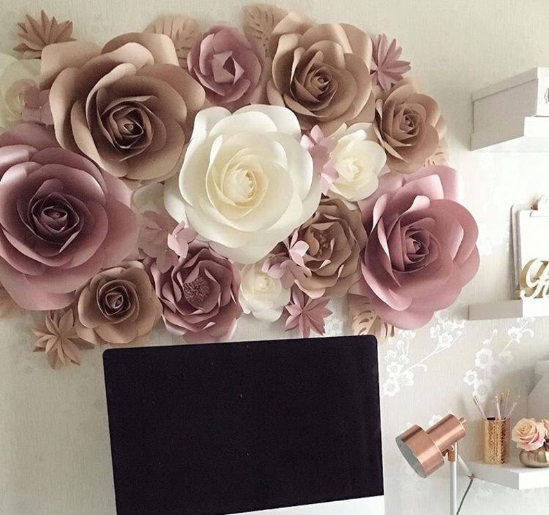 K&ouml;nnte beinhalten: Eine Wand, die mit gro&szlig;en Papierblumen in den Farben Blush-Rosa, Beige und Creme dekoriert ist. Die Blumen sind in einer Gruppe angeordnet und schaffen eine romantische und elegante Atmosph&auml;re.
