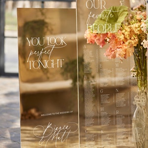 May include: Two mirrored acrylic wedding signs with white calligraphy. One sign reads "You look perfect tonight" and the other lists names. The signs are decorated with flowers and the wedding date.