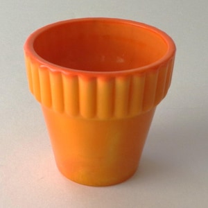 May include: A bright orange ceramic plant pot with a smooth, tapered body and a distinctively ribbed, fluted rim. The glaze features subtle variations in color intensity, transitioning from a deeper orange at the top edge to a lighter hue.