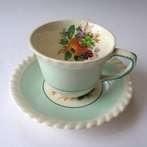 May include: A vintage teacup and saucer set with a light blue and white color scheme. The teacup features a floral design with a fruit motif.