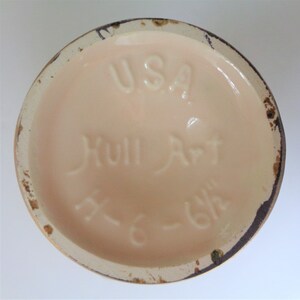 May include: The bottom of a ceramic vase with the words "USA Hull Art" and a number "K-618" in brown lettering on a light pink background.