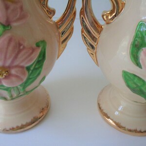 May include: Pair of vintage ceramic vases with a cream base and gold accents. The vases feature raised pink flowers and green leaves.