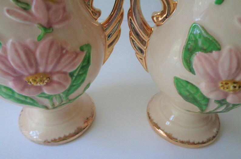 May include: Pair of vintage ceramic vases with a cream base and gold accents. The vases feature raised pink flowers and green leaves.