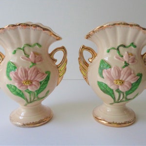 May include: Pair of vintage ceramic vases with pink and green floral designs. The vases have gold accents and ornate handles.