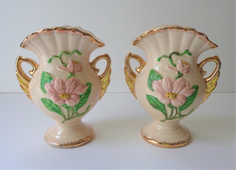 May include: Pair of vintage ceramic vases with pink and green floral designs. The vases have gold accents and ornate handles.