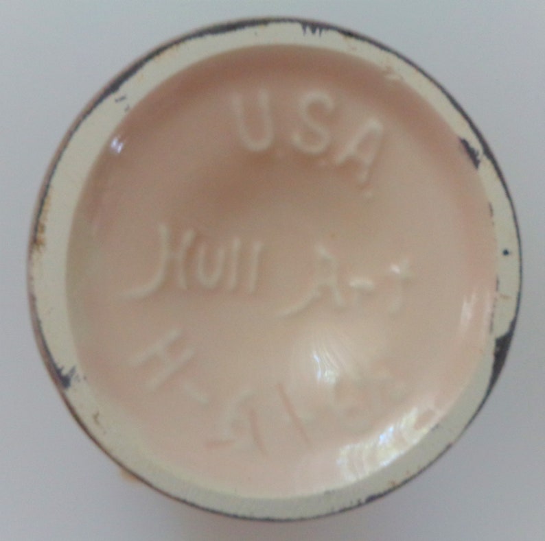 May include: Close-up of the bottom of a pink ceramic mug with the text "Hull Art Pottery" and "USA" in white.