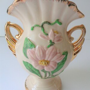 May include: A white ceramic vase with gold trim and floral designs. The vase has two handles and a ruffled top.