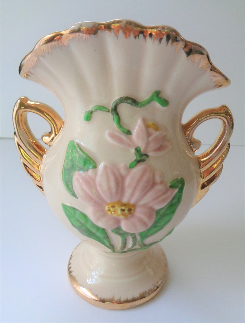 May include: A white ceramic vase with gold trim and floral designs. The vase has two handles and a ruffled top.