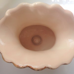 May include: A white ceramic vase with a scalloped rim and gold trim. The vase has a smooth, glossy finish and a round opening at the top.