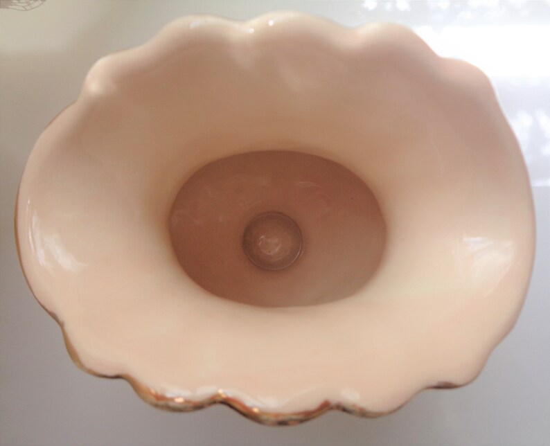 May include: A white ceramic vase with a scalloped rim and gold trim. The vase has a smooth, glossy finish and a round opening at the top.